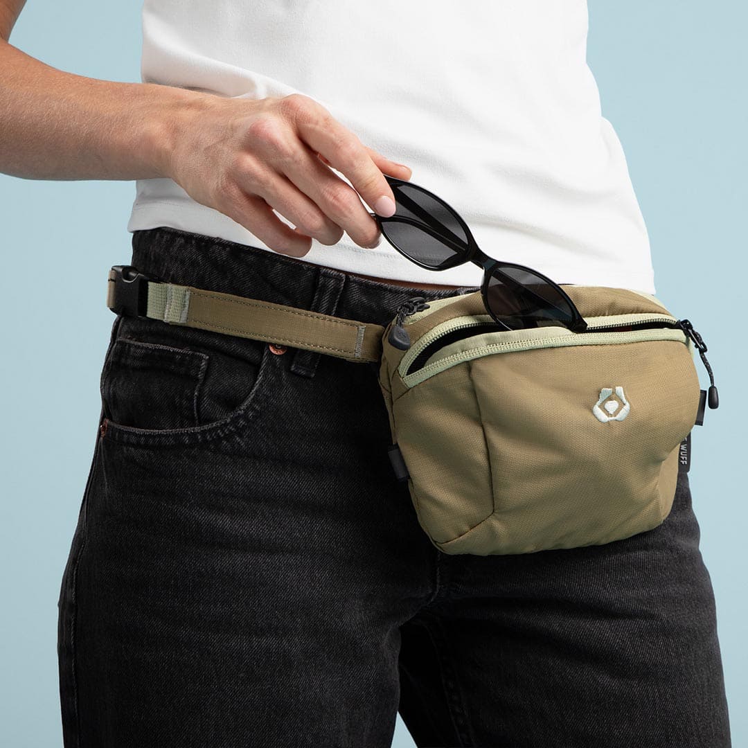 Person wearing a beige waist bag with sunglasses on a light blue background