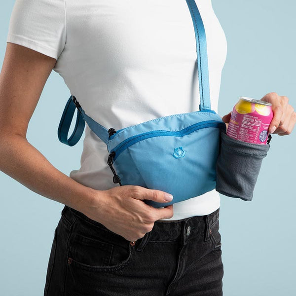 Person wearing a blue waist bag holding a pink can against a light blue background