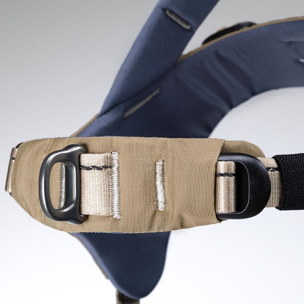 Close-up of a beige seat belt with a black D-ring on a gray background