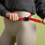 Person holding a red dog leash with a black clip against a green background