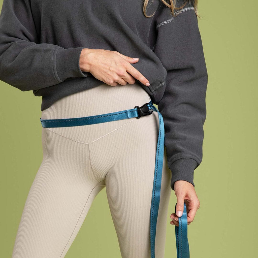 Person wearing a dark gray sweatshirt and beige leggings with a blue belt against a green background