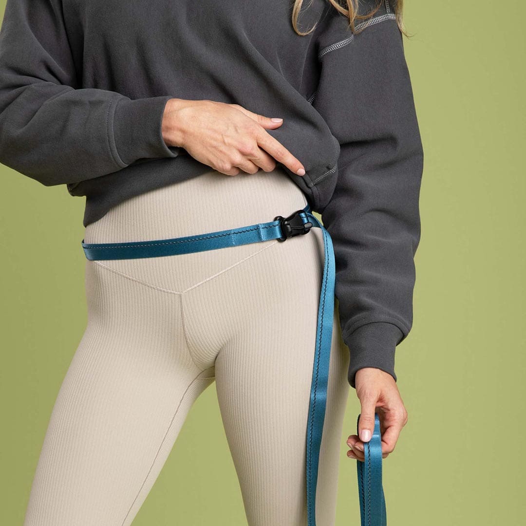 Person wearing a dark gray sweatshirt and beige leggings with a blue belt against a green background