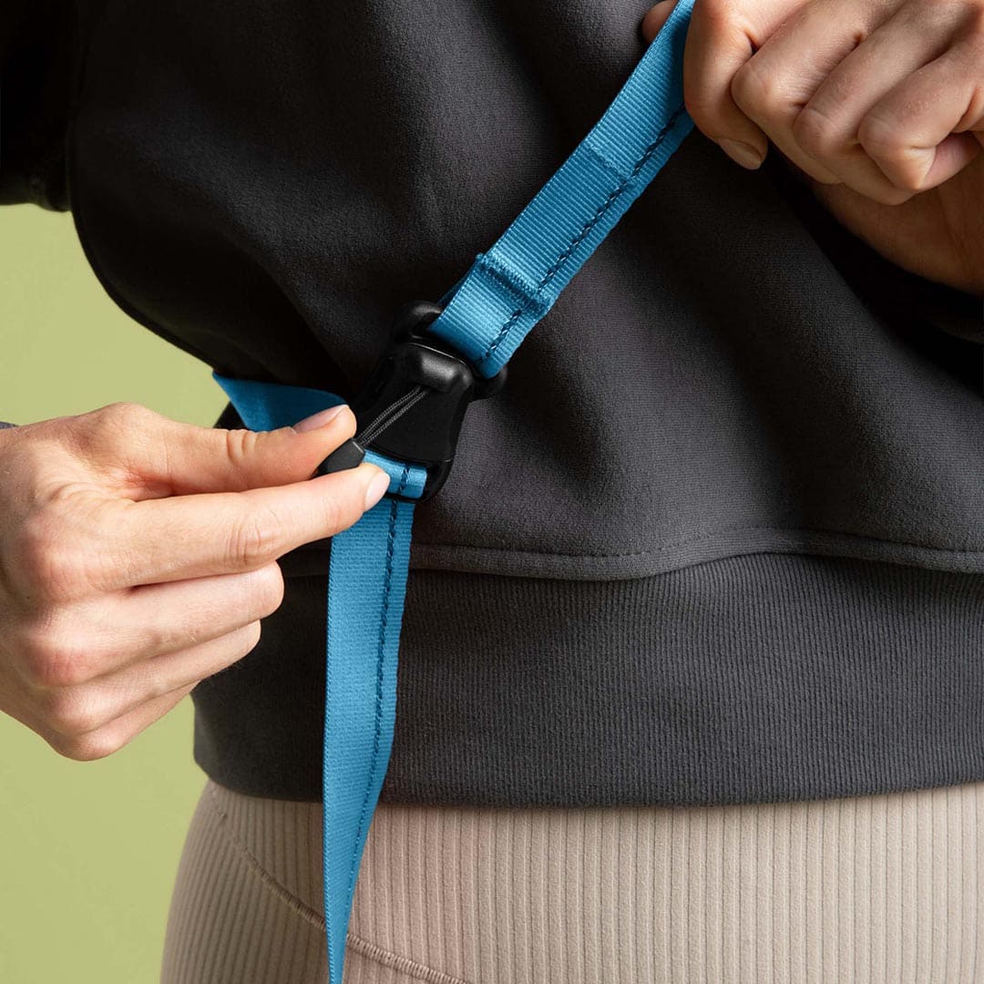 Person adjusting a blue strap on a black bag against a green background