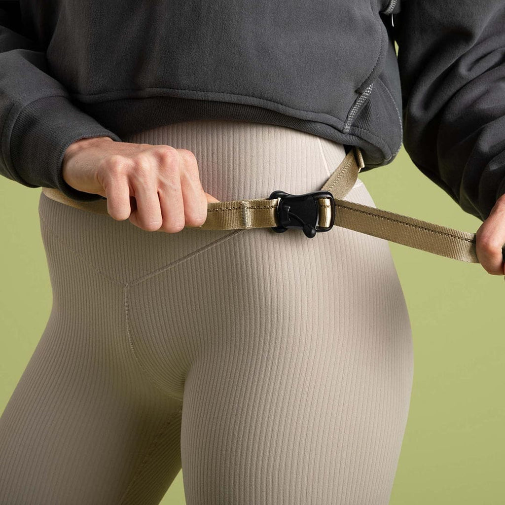 Person adjusting a beige belt with a black buckle on a green background