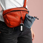 Person wearing a red crossbody bag with a keychain on a pink background