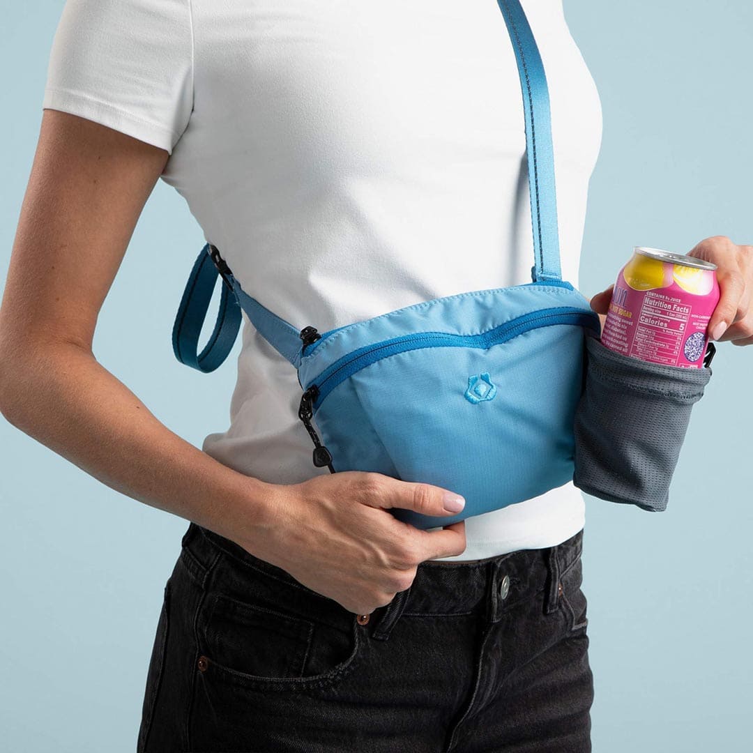 Person wearing a blue fanny pack holding a can against a light blue background