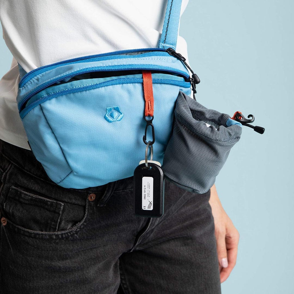 Person wearing a blue crossbody bag with a keychain on a light blue background