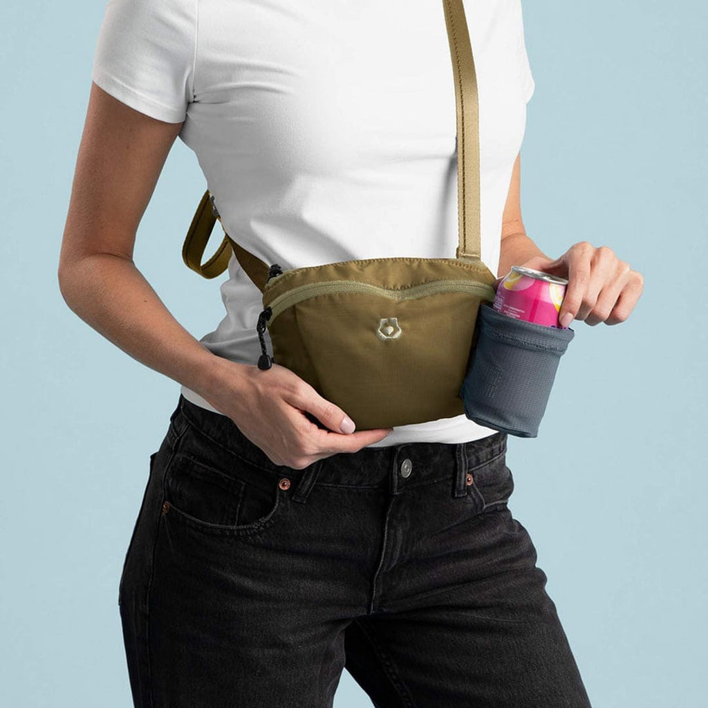 Person holding a green crossbody bag with a small pouch on a light blue background