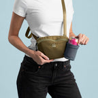 Person holding a green crossbody bag with a small pouch on a light blue background