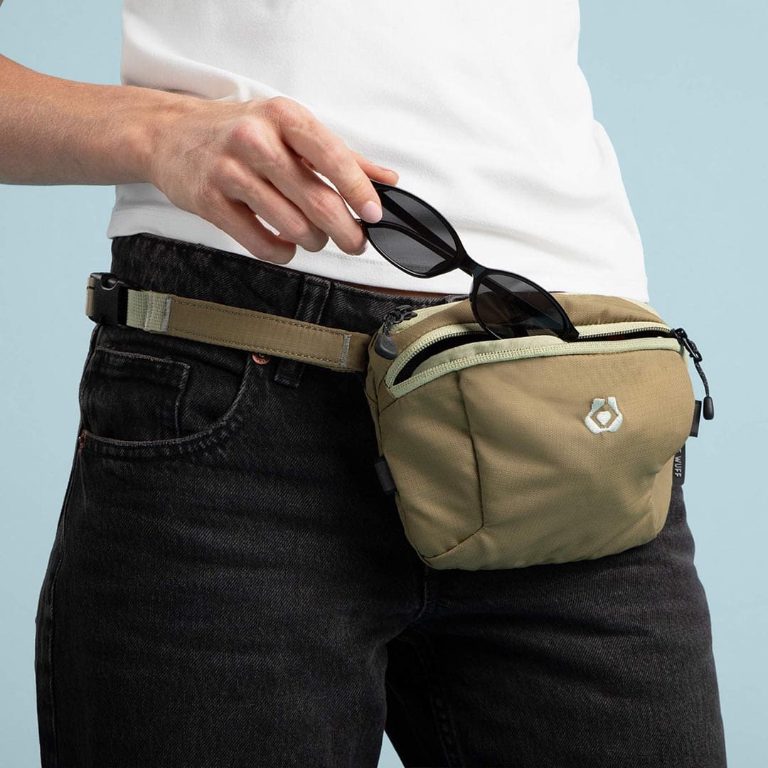 Person wearing a beige waist bag with sunglasses on a light blue background