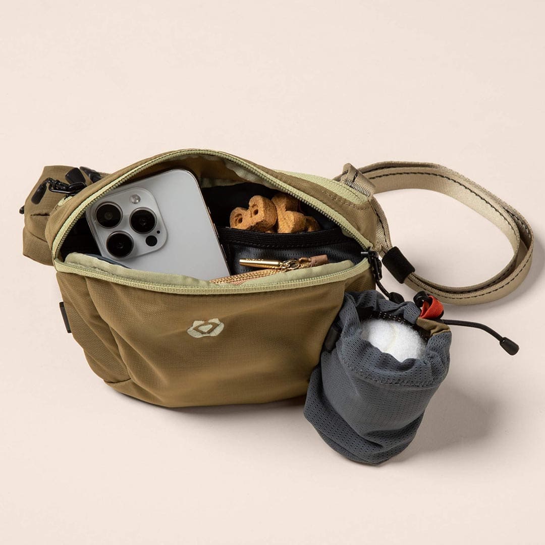 Open brown bag with phone, snacks, and small pouch on beige background