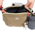 Beige pouch with sunglasses and keys, held by a hand against a white background