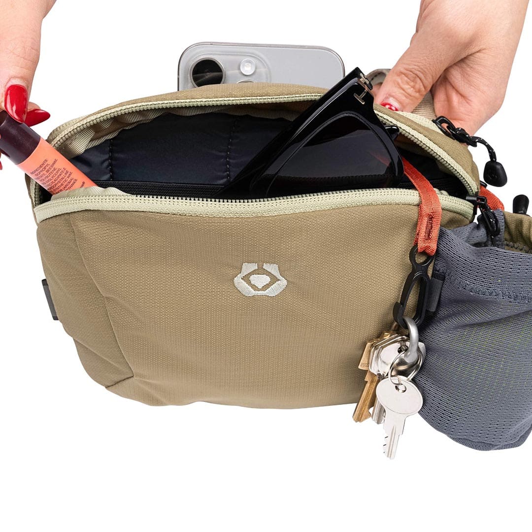 Beige pouch with sunglasses and keys, held by a hand against a white background