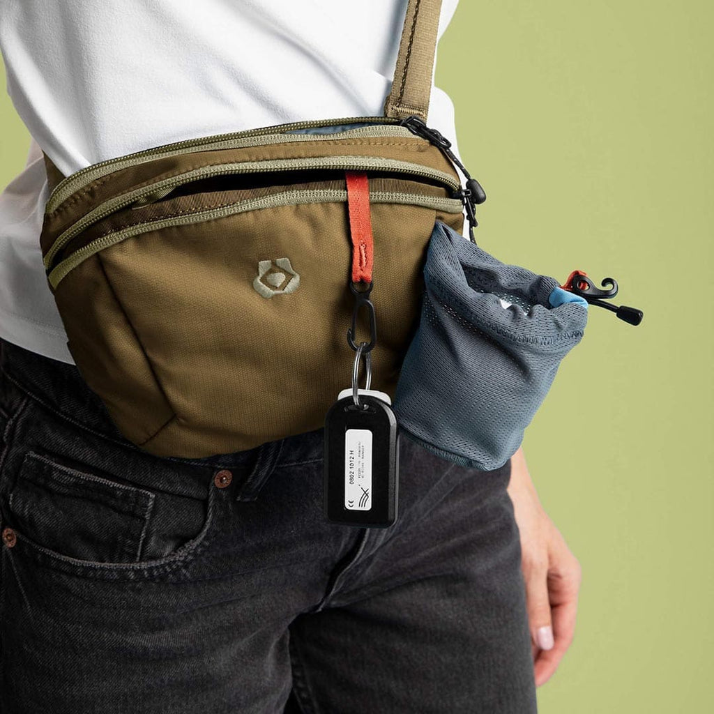 Person wearing a brown crossbody bag with a visible brand logo on a green background