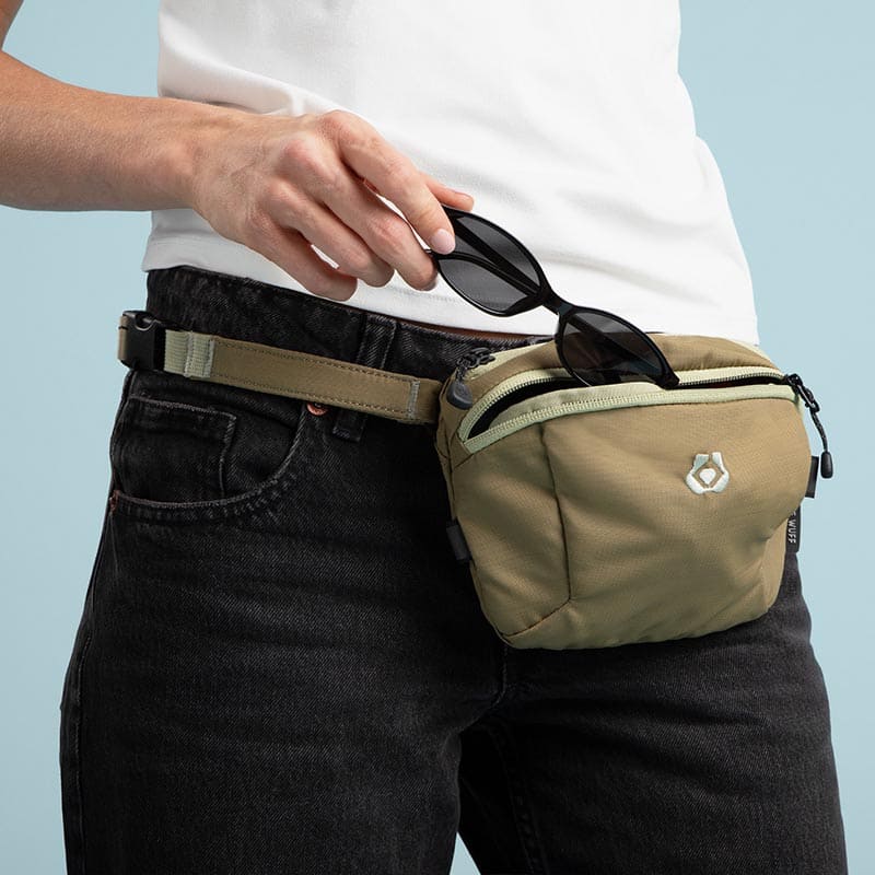 Person wearing a beige waist bag with sunglasses on a light blue background